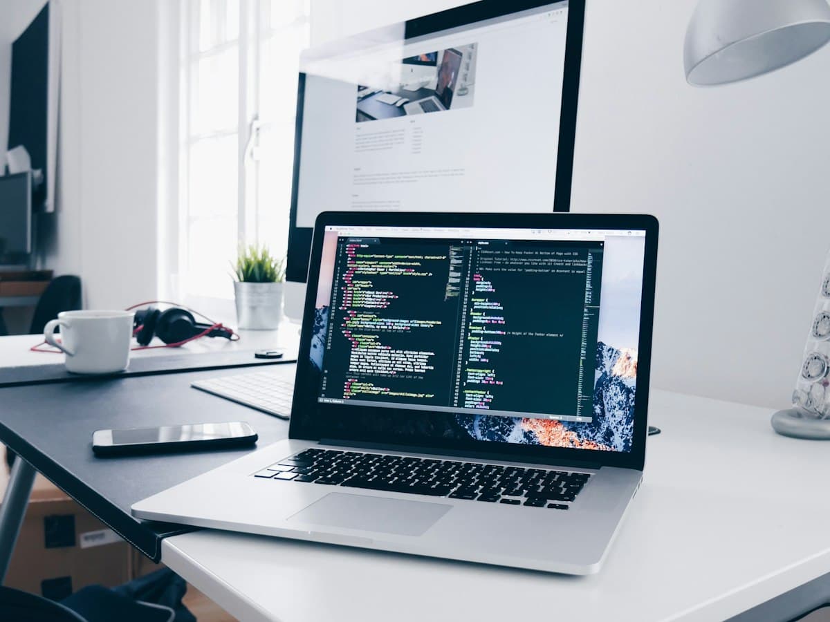 Laptop displaying source code on a clean desk next to a desktop monitor